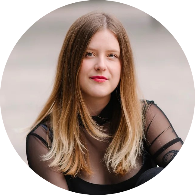 Lisa Wölfl sieht direkt in die Kamera. Sie sitzt im Freien vor einem grauen Hintergrund.