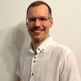 Benedikt Schmidt Auf dem Bild ist Benedikt Schmidt, lächelnd mit weißen Hemd zu sehen