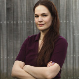 Nina Bömelburg Die Kandidierenden schaut freundlich und gleichzeitig, hoffnungsvoll und bestimmt in die Kamera. Ihre Arme sind verschränkt. Sie hat lange rotbraune Haare.