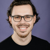 Laurin Brinkmann Das bild ist ein Portrait von mir. Ich habe lange dunkle Haare, braune Augen und einen kurzen Bart. Außerdem trage ich eine schwarze Brille und ein schwarzes T-Shirt.