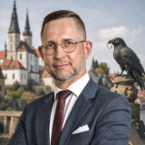 Daniel Wald Daniel Wald im dunkelblauen Anzug mit weißem Hemd und bordeauxfarbener Krawatte. Im Hintergrund sind der Merseburger Dom und Schloss, sowie eine Rabenstatue aus der Rabensage, mit dem Ring zu sehen.