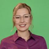 Portrait Andrea Franz: freundliches Lachen, unaufdringliche Brille, locker zurückgesteckte Haare, lila Hemd.