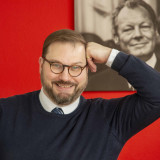 Jens Fischwasser vor rotem Hintergrund und Bild von Willy Brandt