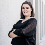 Porträtfoto von Jasmin Weber, stehend vor einer hellen Gebäudefassade, mit verschränkten Armen.