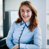 Melanie Nerlich, lächelnd und mit schickem Oberteil auf einem Bürosessel