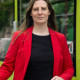 Eine junge Frau steht mit einem Fahrrad vor einer Straßenbahn der Magdeburger Verkehrsbetriebe. Sie trägt ein rotes Sakko und ein schwarzes T-Shirt. Die langen Haare sind offen.