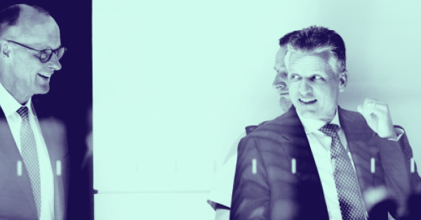 Friedrich Merz (links) und Thorsten Frei (rechts) in Anzug und Krawatte während eines Gesprächs. Das Foto ist durch eine Glasscheibe aufgenommen und in einem blaugrünen Farbton gestaltet.