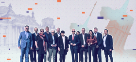 Auf dem Bild zu sehen: Eine Gruppe an Personen, vor allem Bundestagsabgeordnete, die in die Kamera sehen. Im Hintergrund stilisiert der Bundestag und eine Rakete.