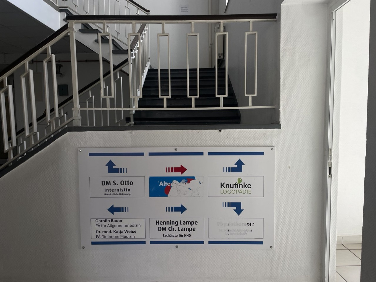 Zu sehen sind Wegbeschreibungen innerhalb des Gebäudes zu den verschiedenen Ärzt:innen, sowie zur AfD, wobei das Schild der Partei beschädigt ist.